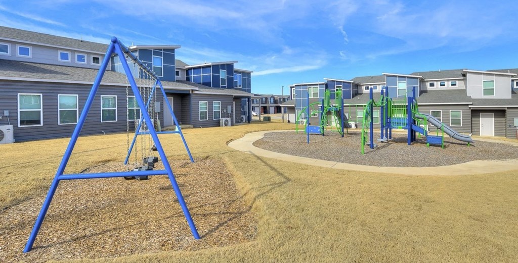 A playground with a blue swing set in the foreground and apartment buildings in the background.