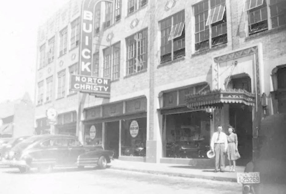 A black and white photo of a couple standing outside a store with the sign "Norton Christy".