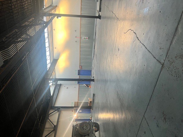 A large industrial machine is in the foreground of a room with a concrete wall.