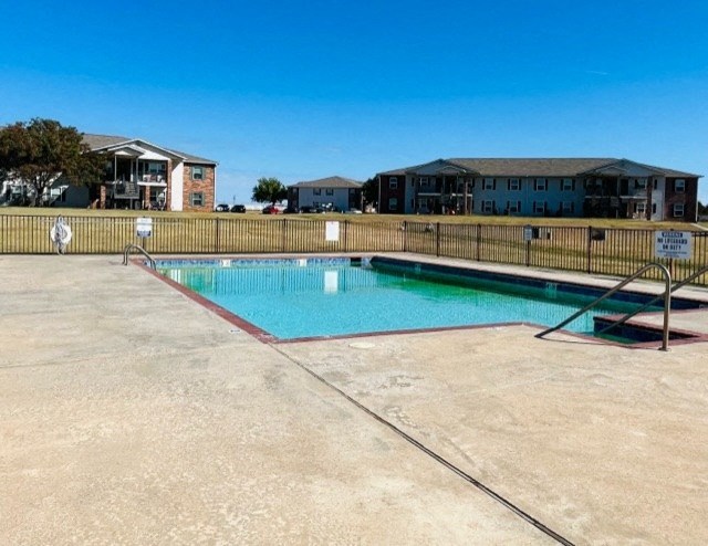 a pool with a fence and apartments in the background