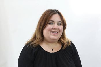 A woman with a black top and a necklace is smiling.
