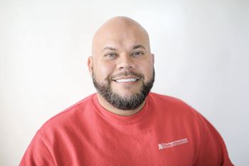 A man with a beard wearing a red shirt with a logo on it.