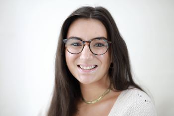 A woman with glasses and a necklace is smiling.