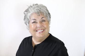 A woman with short grey hair and a black shirt is smiling.