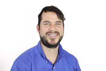 A man with a beard and short hair is wearing a blue shirt.