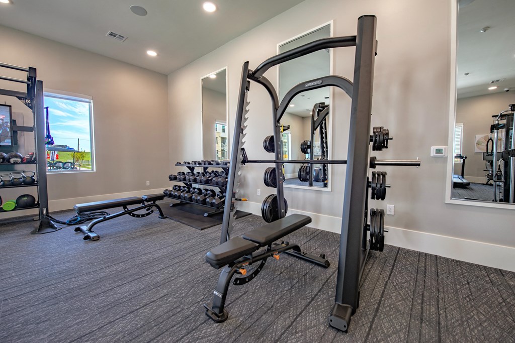 a gym with weights and cardio equipment and a large mirror
