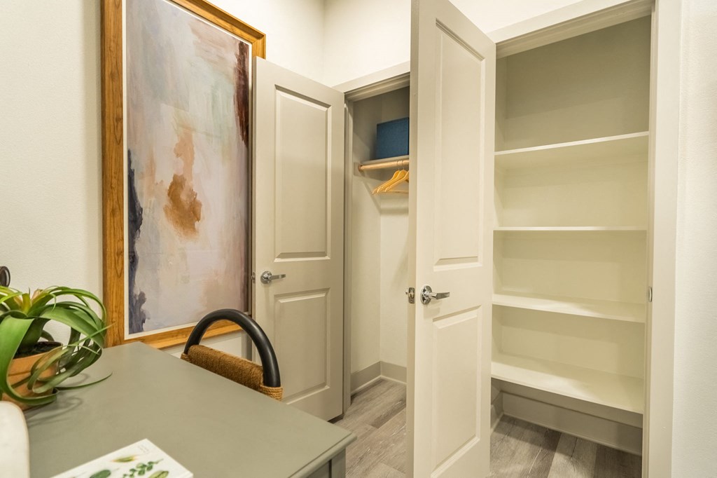 a closet with white doors and shelves and a table with a chair