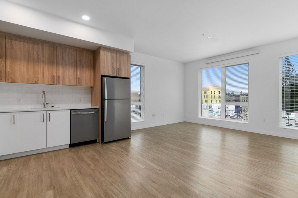 an empty living room with a kitchen and a large window