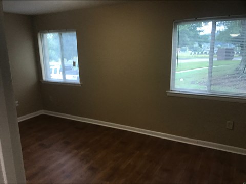 an empty living room with wooden floors and two windows