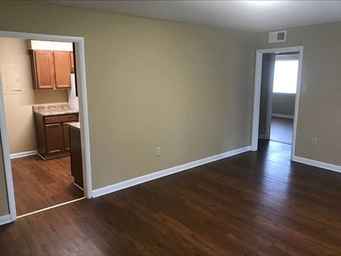 an empty living room with wood floors and a kitchen