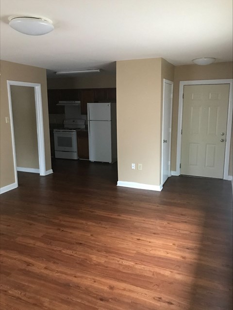 an empty living room with wood floors and a kitchen