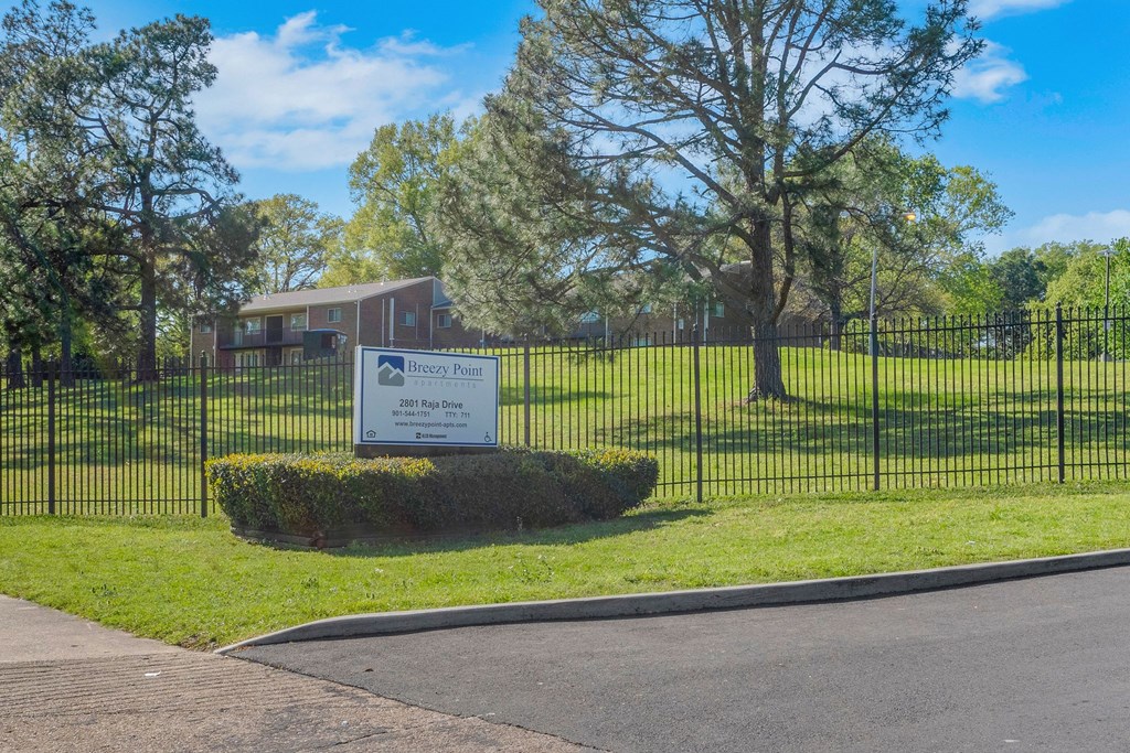 A sign sitting in front of a fence and green trees.