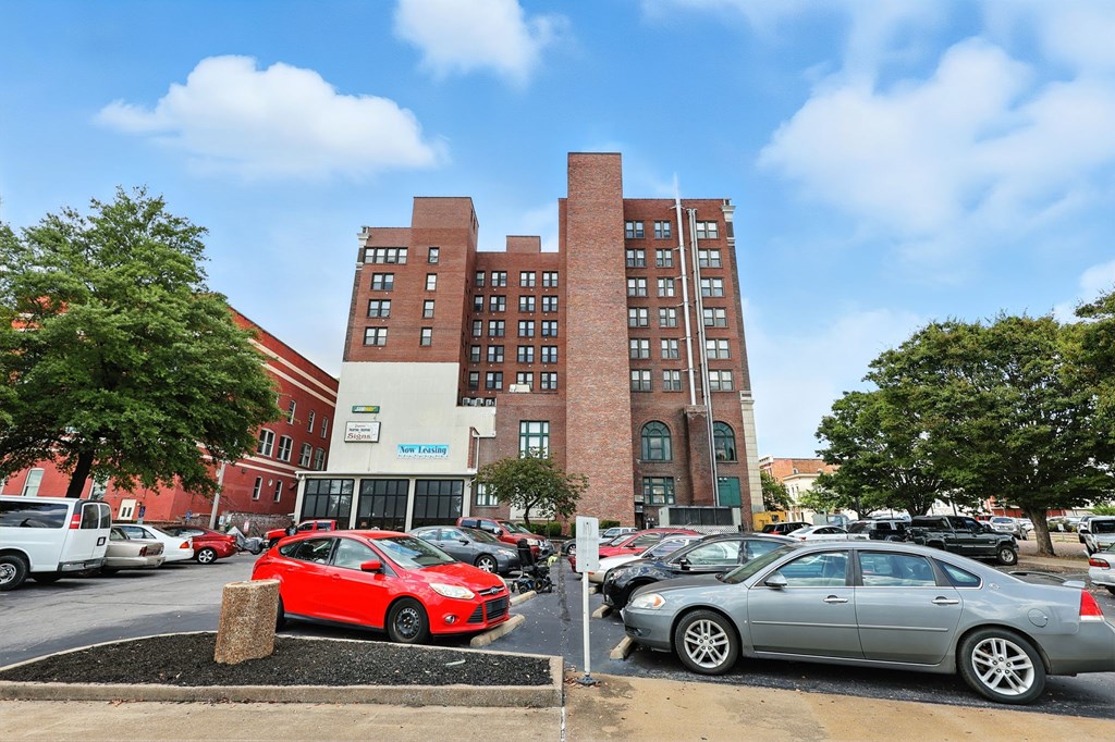 A parking lot with cars and a tall red brick building in the background.