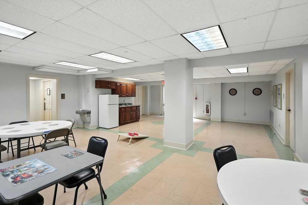 A room with tables and chairs and a white fridge.