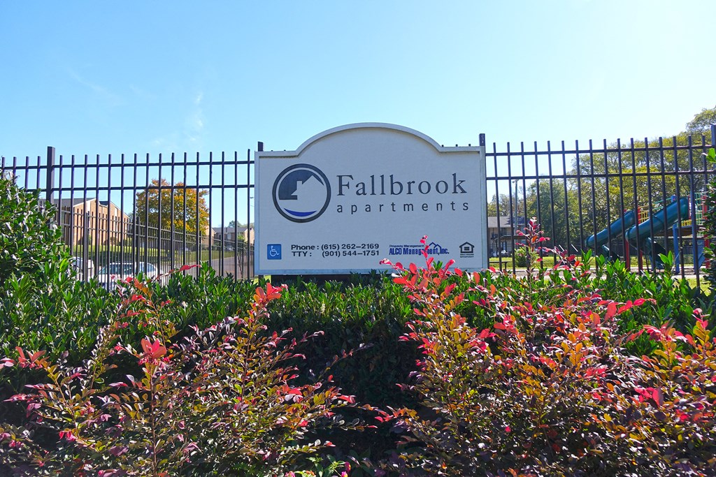 a sign for fallbrook apartments in front of a fence and flowers