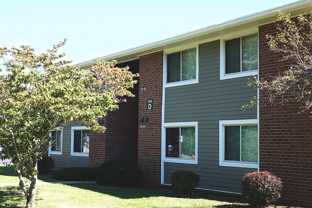 the front of a brick apartment building with a lawn and trees