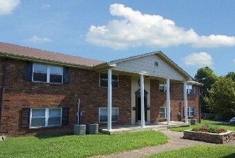 A brick building with a porch and a green lawn in front.