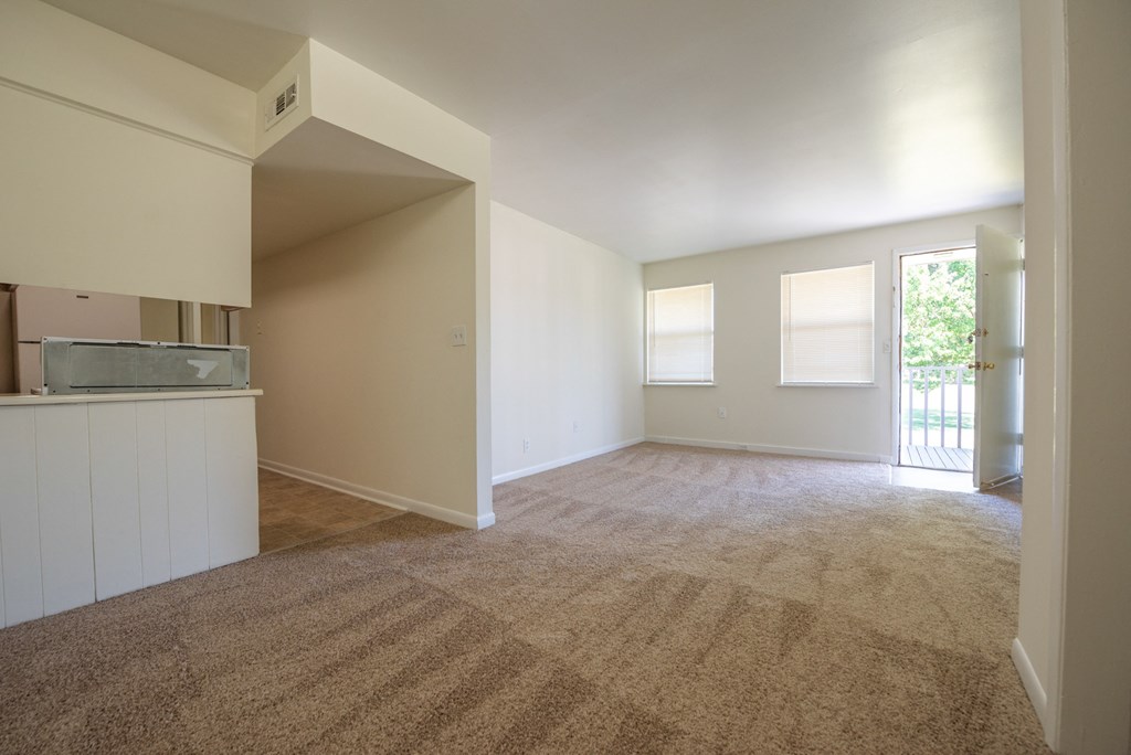 an empty living room with a kitchen in the background