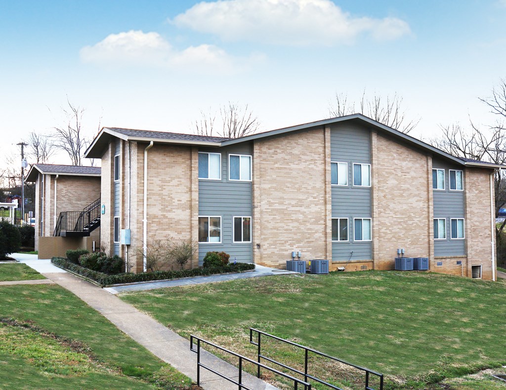 an apartment building with a green lawn and a sidewalk