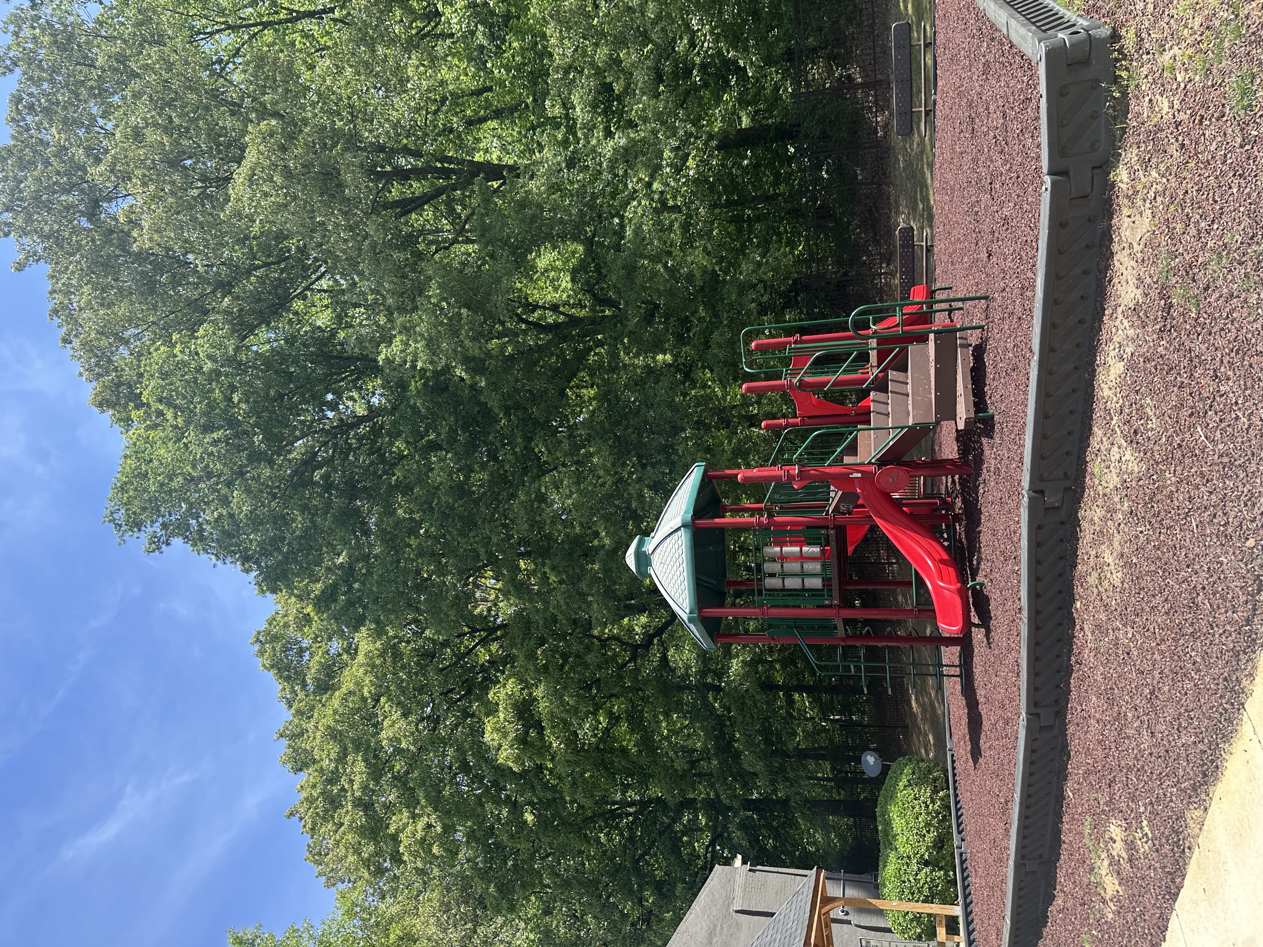 A red playground in front of  trees.