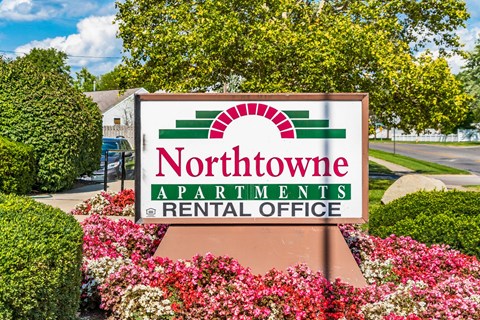 A sign for Northtowne Apartments Rental Office is displayed in front of a flower bed.