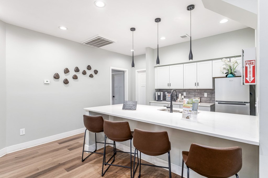 A kitchen with white countertops and brown chairs.