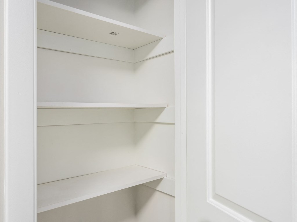 a walk in closet with white shelving and a window