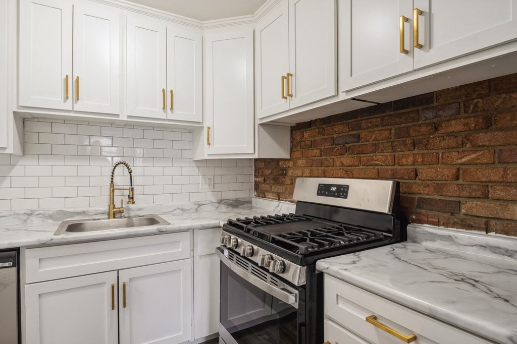 a kitchen with white cabinets and a brick wall