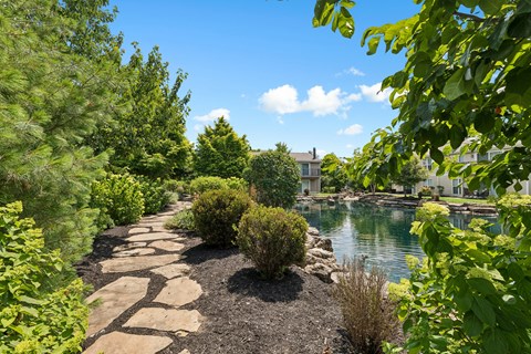 A stone pathway leads through a garden to a body of water.