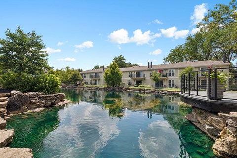 A serene pond in front of a house with a deck.