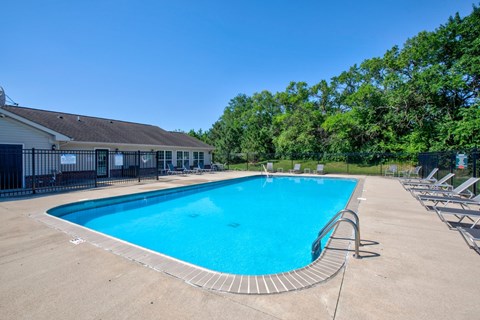A large outdoor swimming pool surrounded by a fence and lounge chairs.
