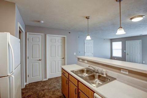 A kitchen with a white fridge, brown carpet, and a white sink.
