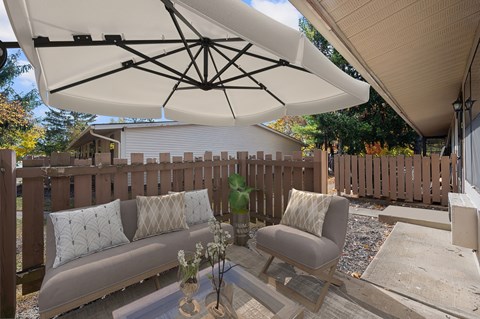 A patio with a white umbrella and a grey couch.