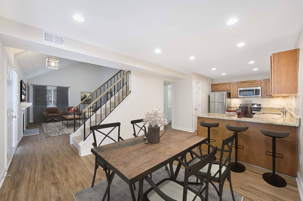 a dining area with a wooden table and chairs and a kitchen with a staircase in the background at Harpers Point Apartments, Cincinnati, Ohio