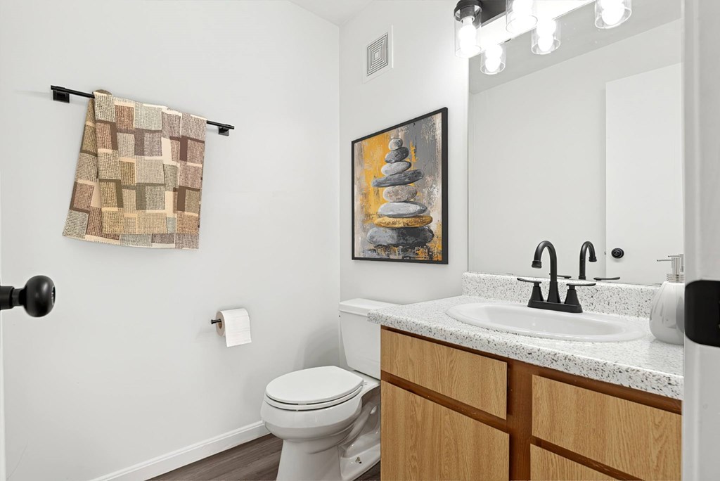 A bathroom with a toilet, sink, and a painting on the wall.