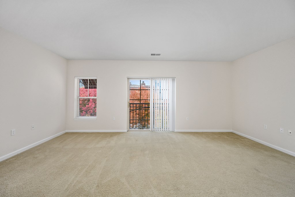 a spacious living room with carpet and a door to a balcony