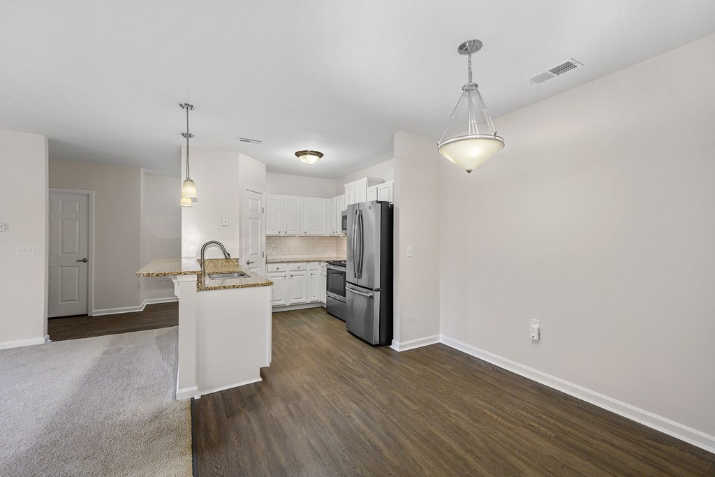 an empty living room with a kitchen with stainless steel refrigerator and