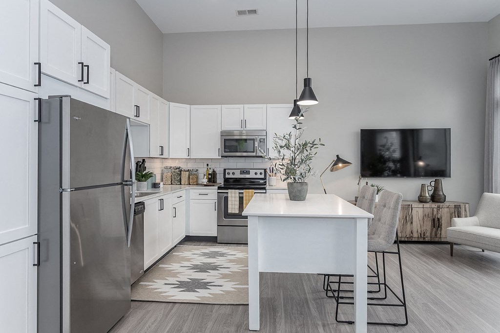 Liberty Township, OH, Apartments Near Paul Brown Stadium - Liberty Center - Modern Kitchen with Vinyl Wood Plank Flooring, Stainless Steel Appliances, White Quartz Countertops, White Cabinetry, Tile Backplash, Moveable Island with Grey Chairs, Pendant Lights, and Access to Living Room.