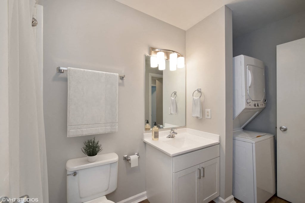 a bathroom with a toilet sink mirror and a washer and dryer