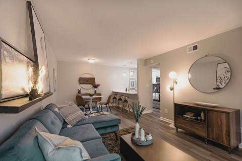 A living room with a grey couch and a round mirror on the wall.