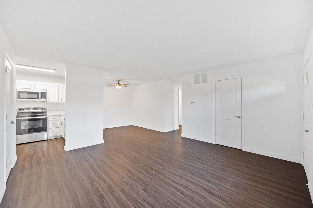 the living room and kitchen of an apartment with wood flooring and white walls