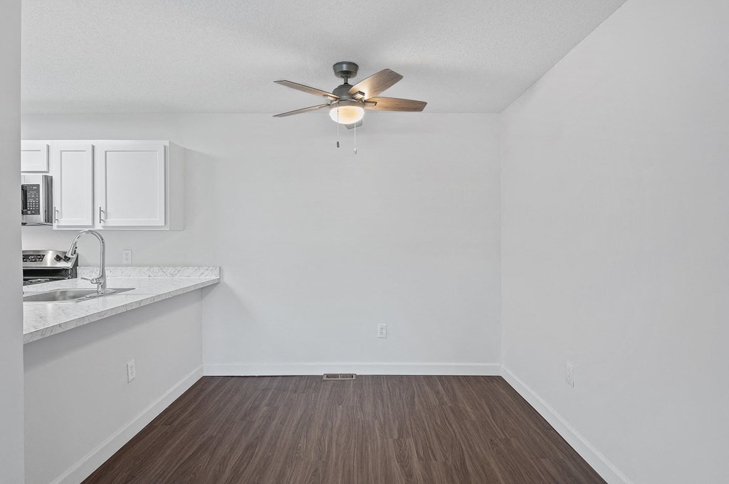 an empty living room with a ceiling fan and a kitchen
