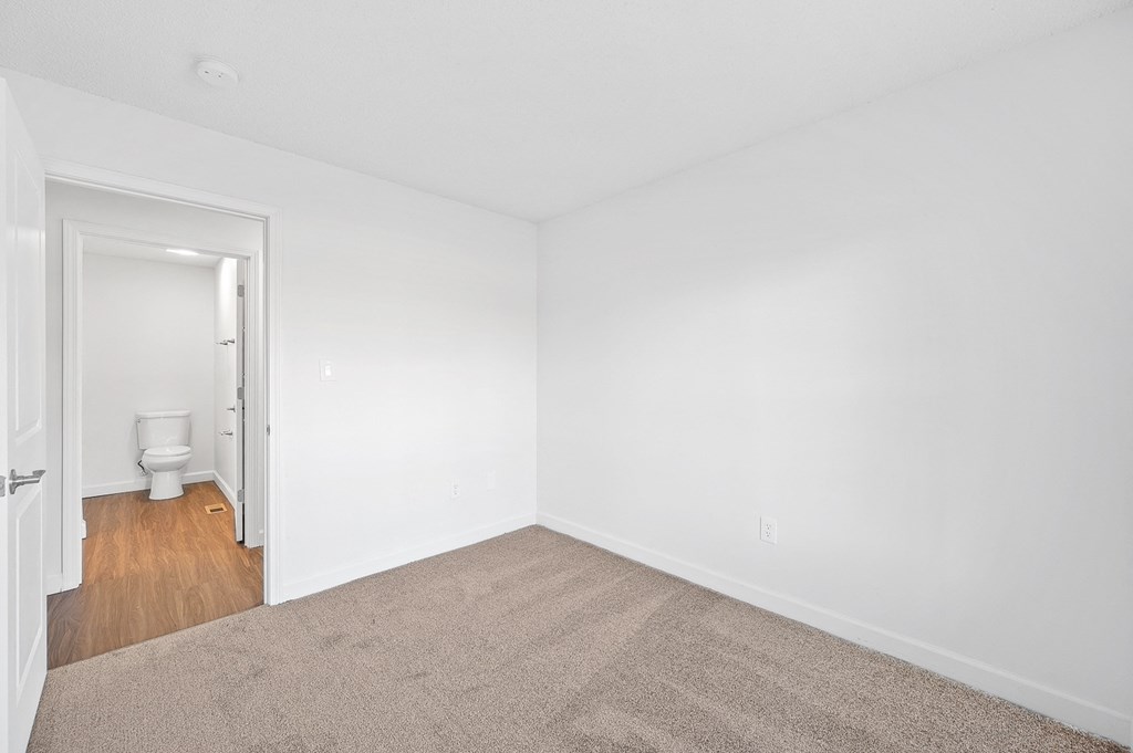 a bedroom with white walls and carpet and a bathroom with a toilet