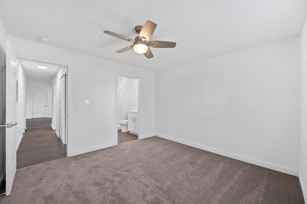 an empty living room with a ceiling fan and a hallway