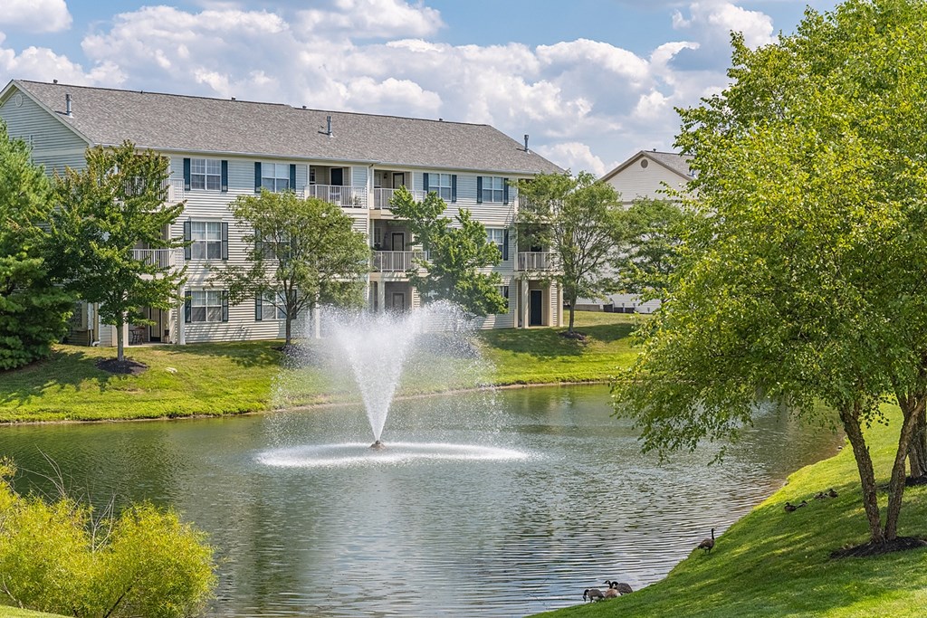 a fountain in the middle of a lake with a building in the background at Bishops Gate, Cincinnati, OH