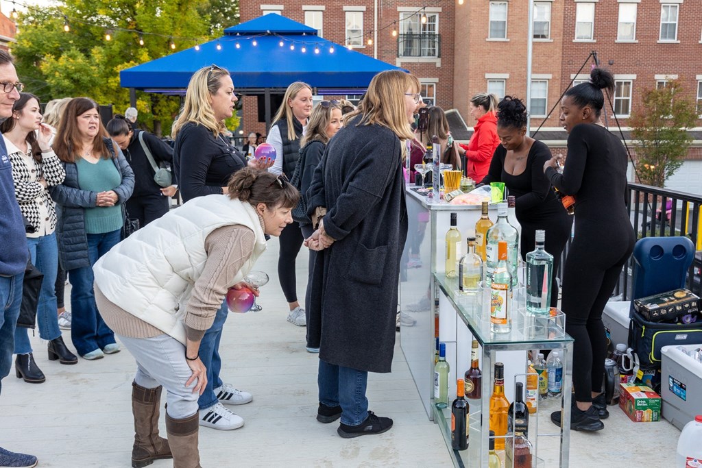 a group of people standing around a table with bottles of alcohol