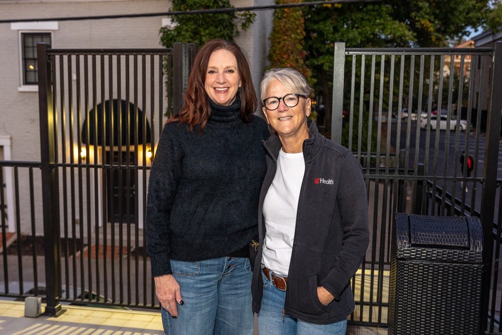 two women standing next to each other in front of a fence