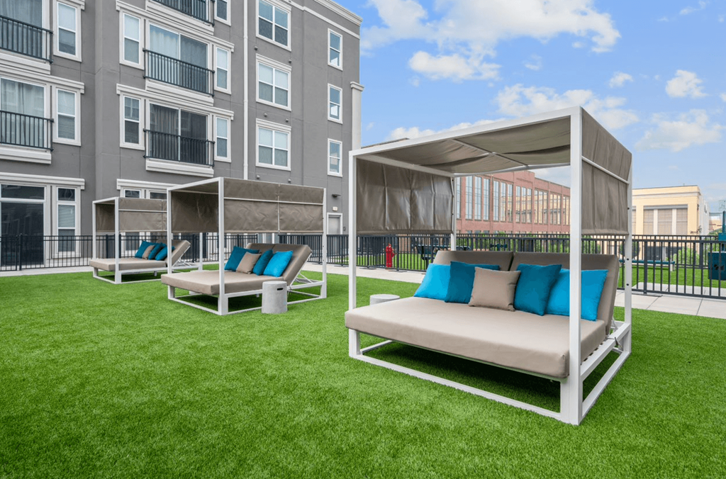 a patio with couches and chairs on a lawn in front of an apartment building
