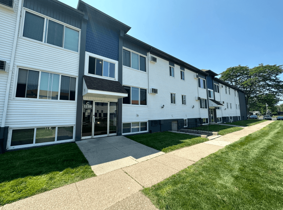a large white building with a blue roof and a sidewalk in front of it
