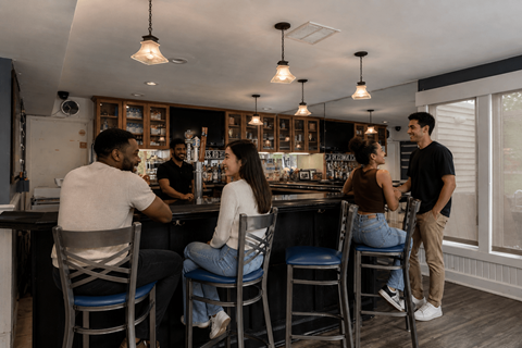 A group of people are gathered in a bar with a bartender behind the counter.
